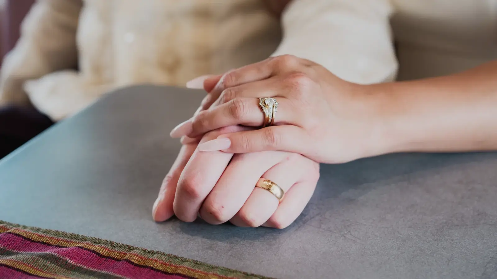 Deux mains jointes sur une table, avec alliances